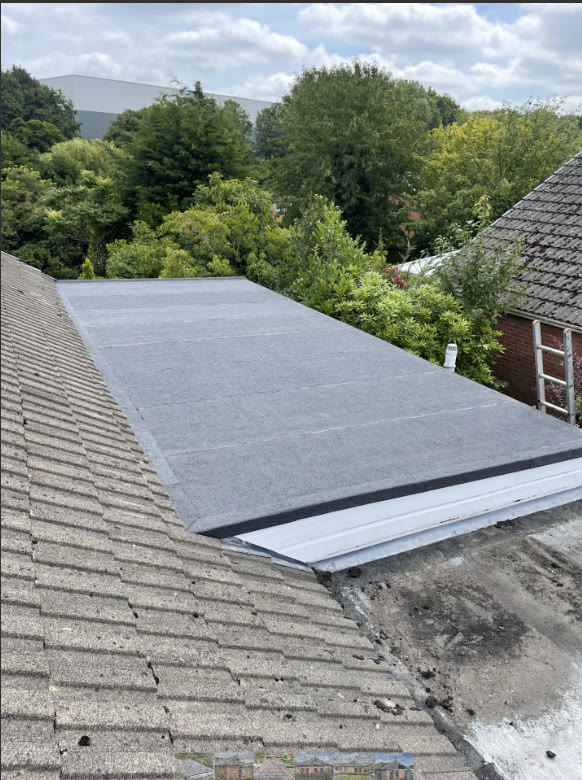 New dark mineral-felt flat roof with white fascia against an older tiled pitch