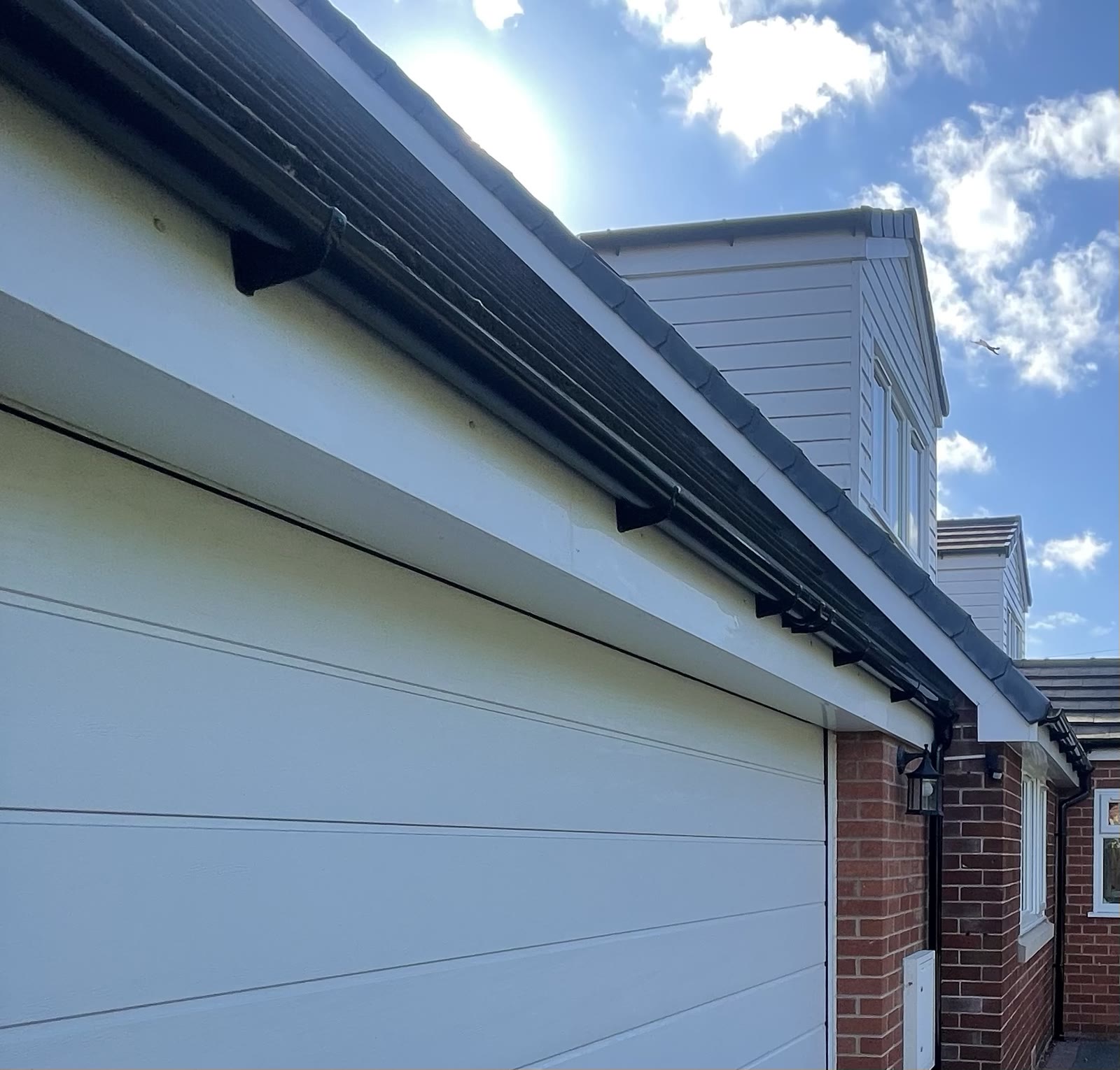White fascia, black gutter and dark tiles on a brick house with a dormer