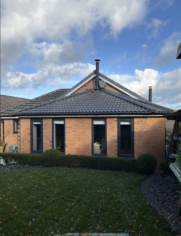 Dark grey hip roof on a red-brick house extension with black guttering