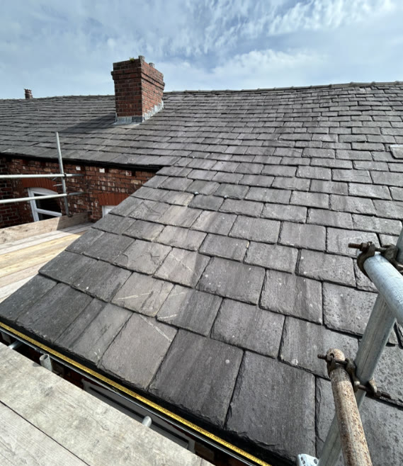 Grey slate roof and brick chimney with a measuring tape on the scaffold